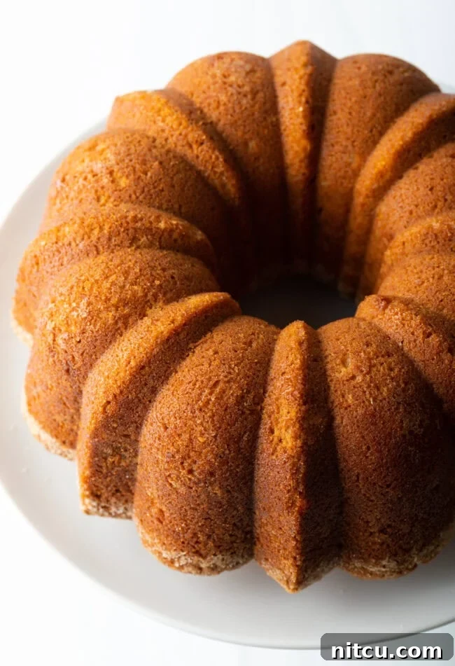 Baked sweet potato pound cake on a white cake stand, showcasing its golden-brown crust and elegant Bundt shape.