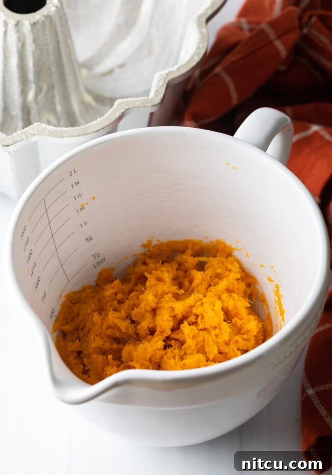 Cooked and mashed sweet potatoes, a vibrant orange, presented in a white measuring bowl, ready for mixing.