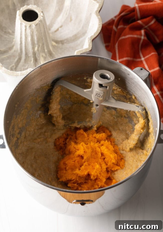Rich cake batter with streaks of sweet potato mash being blended in a mixing bowl with a paddle attachment.