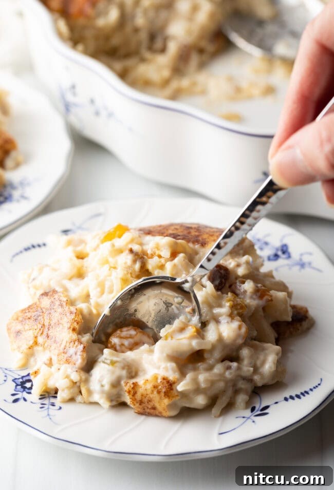 A metal spoon delicately scooping a bite of luscious rice pudding from a white plate, highlighting its creamy texture and comforting appeal.