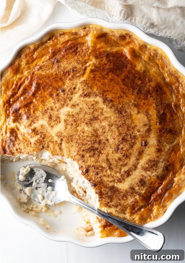 Overhead view of a perfectly baked rice pudding in a beautiful circular dish, a metal spoon having scooped out a generous portion, revealing its rich, creamy texture.