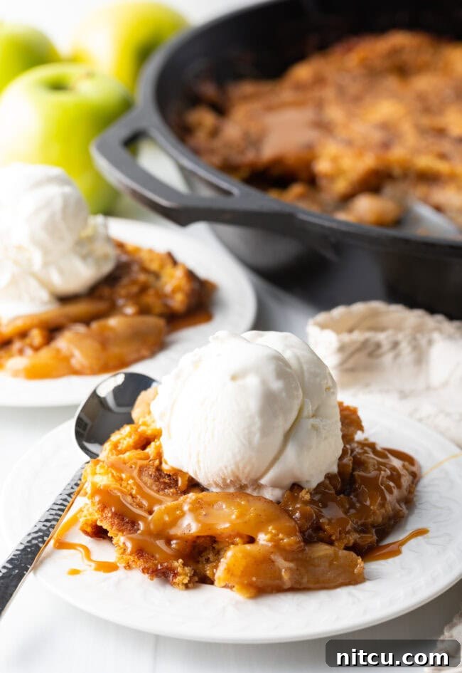 A charming scene of a portion of Caramel Apple Dump Cake on a white plate, accompanied by a scoop of vanilla ice cream and a spoon, inviting a delicious bite.