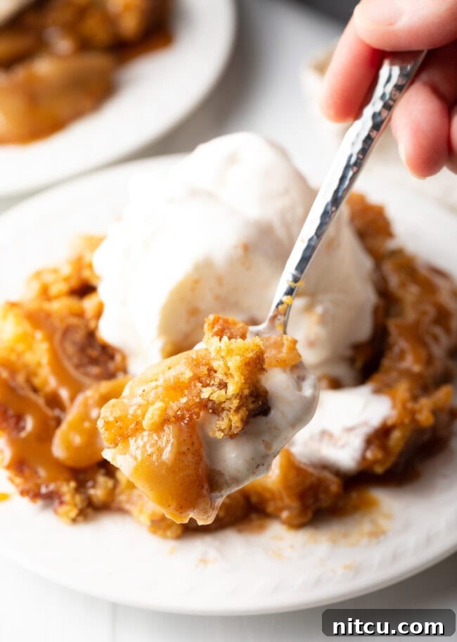 A spoon holds a perfect bite of warm Caramel Apple Dump Cake, presenting it enticingly towards the camera.