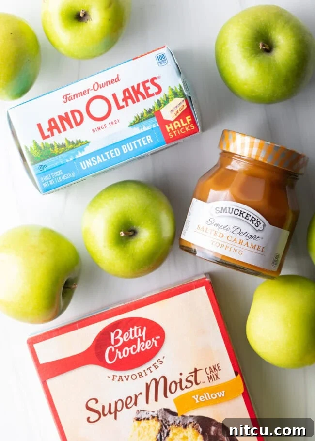 A vibrant top-down view of the core ingredients for Caramel Apple Dump Cake: sticks of unsalted butter, crisp Granny Smith apples, a jar of salted caramel sauce, and a box of classic yellow cake mix.