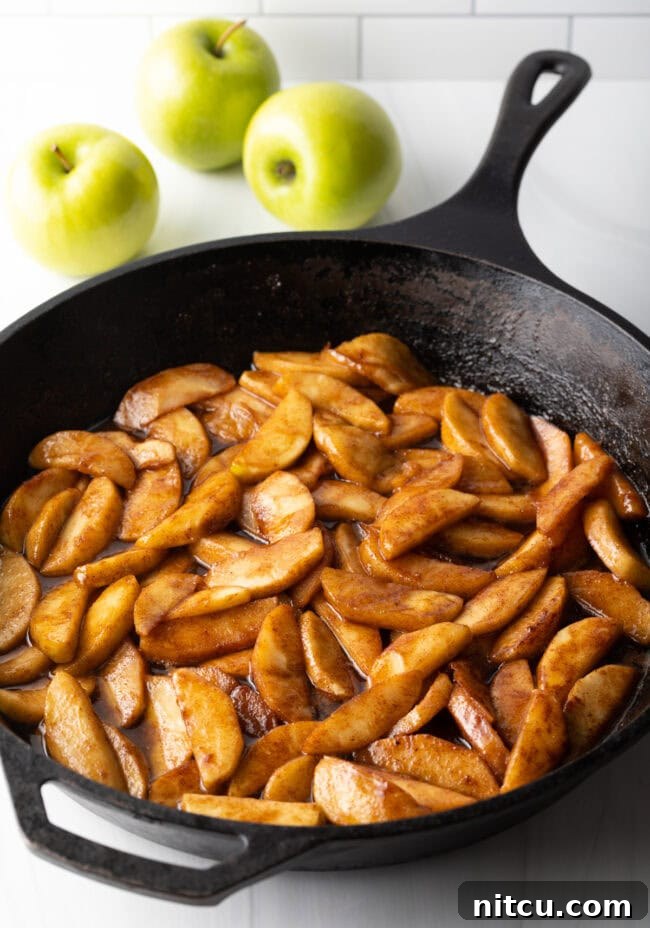 Perfectly cooked and spiced apple slices shimmer invitingly in a cast iron skillet, forming the delicious base of the dump cake.