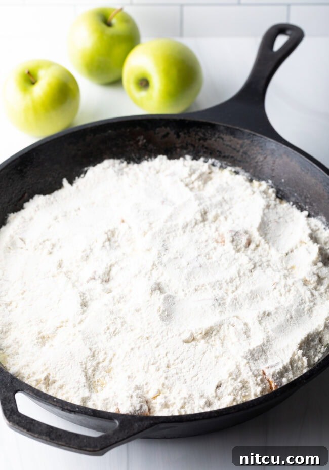 Dry powdered cake mix evenly sprinkled over the softened, spiced apple filling in a cast iron skillet, ready for butter and baking.
