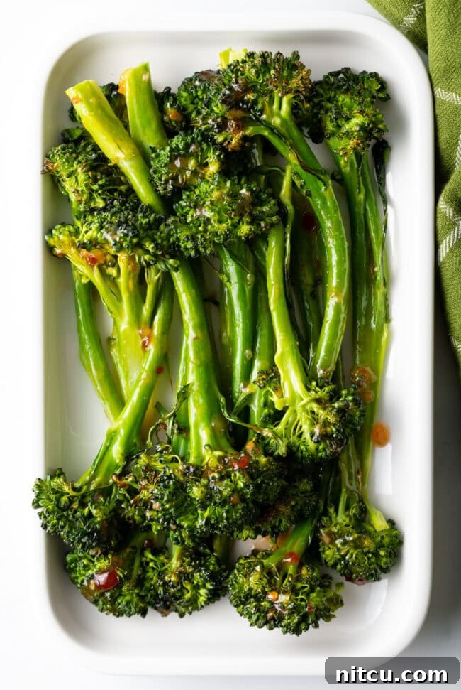Top down oven roasted broccolini recipe with sweet chili glaze stacked on a white rectangle serving platter.