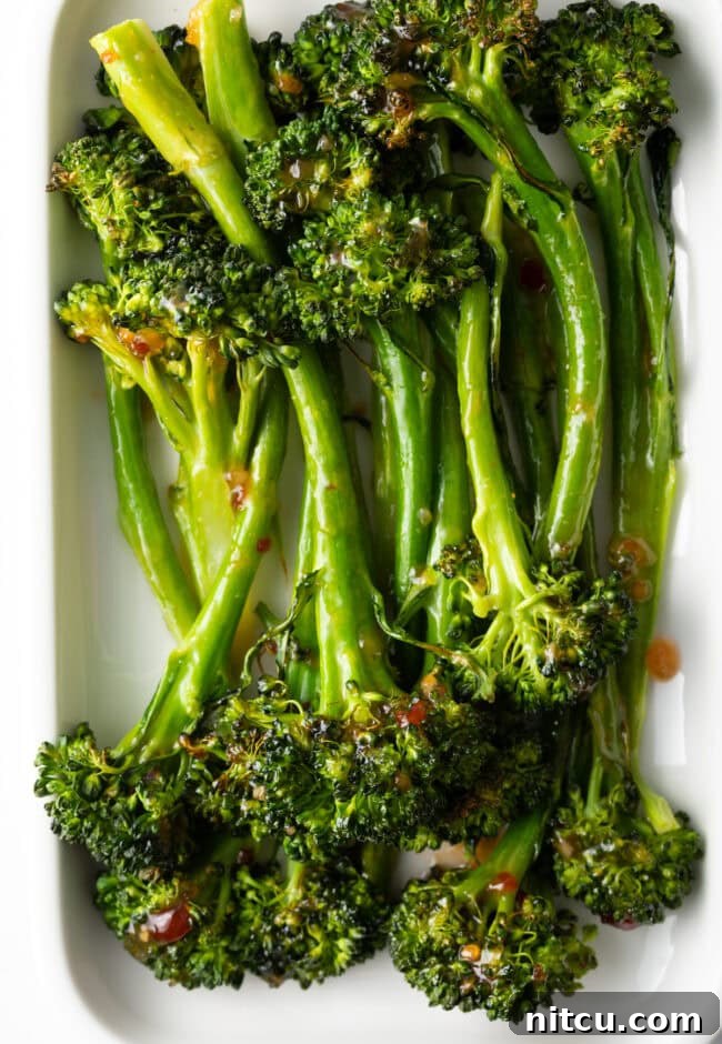 Roasted broccolini recipe finished - with sweet chili glaze stacked on a white rectangle serving platter.