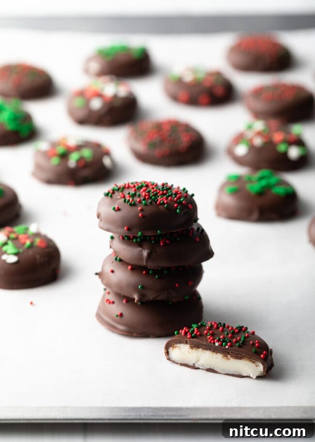 Four peppermint patty candies stacked on top of each other, fifth piece with bite taken out. Rows of more candies in the background.