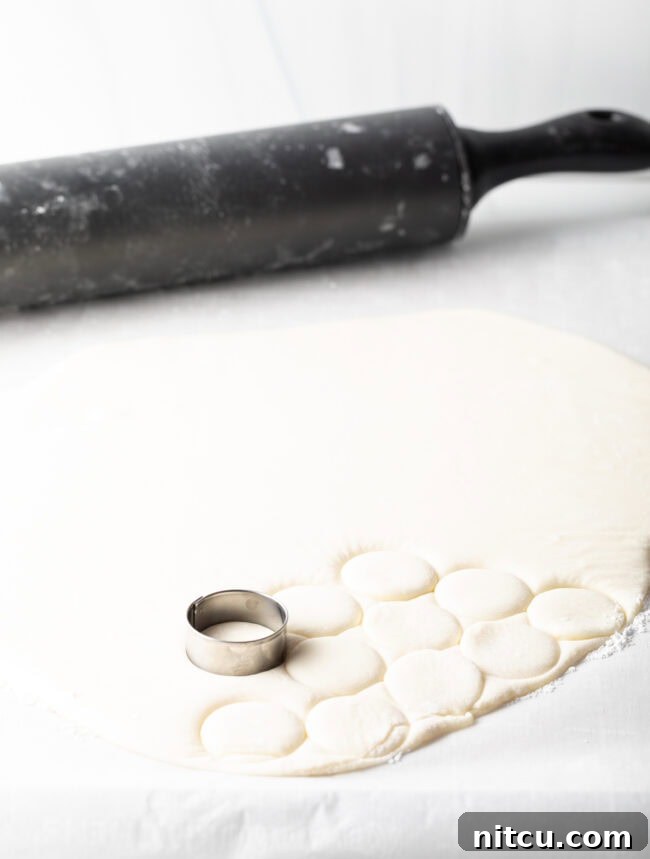 Patty dough rolled out in a sheet, 1-inch metal round cookie cutter making small circles.
