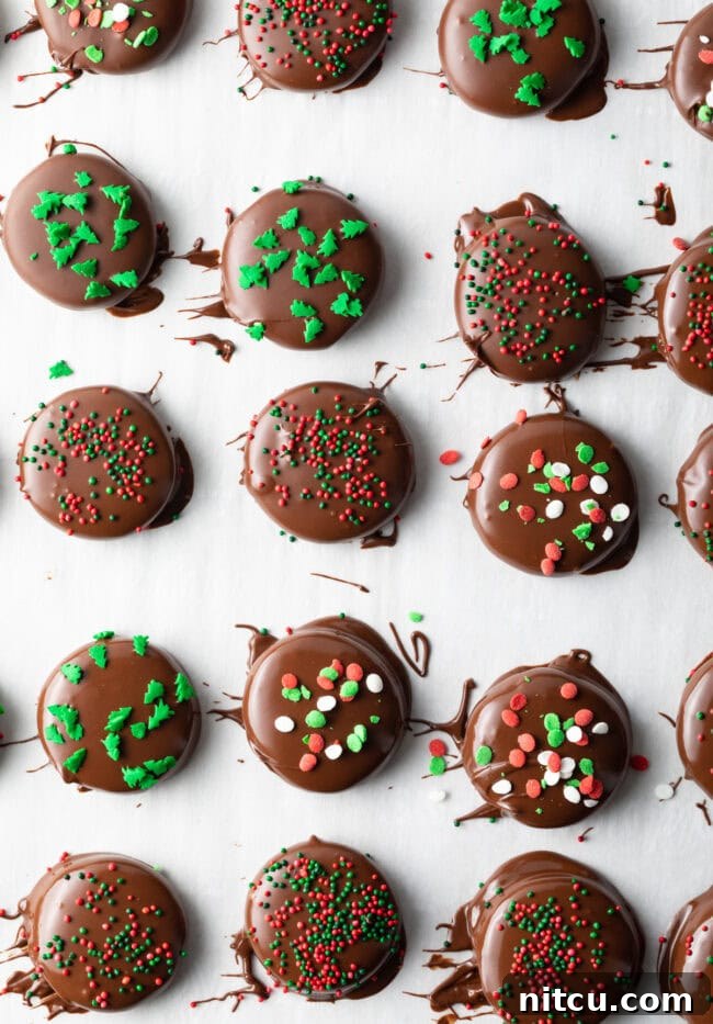 Dipped peppermint patties on parchment paper, sprinkled with green and red candies.