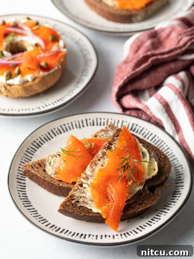 Two slices of pumpernickel bread with butter and pieces of gravlax on top, garnished with fresh dill.