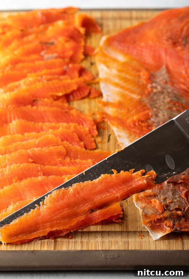 Closeup of a sharp knife expertly cutting thin slices of cured gravlax against the grain.