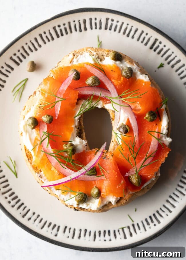 Top down view half of a bagel with cream cheese, smoked gravlax, capers and sliced red onions, a quintessential breakfast.