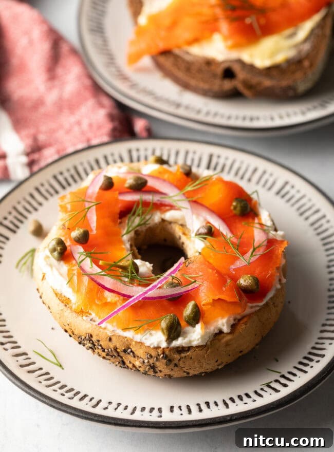 Half a bagel on a plate, with cream cheese, slices of lox, capers and sliced onions, ready to be enjoyed.