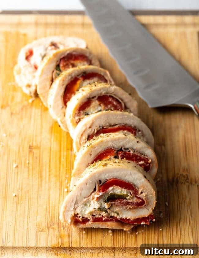 Stuffed chicken roulade, thin sliced on a cutting board with large knife, revealing the beautiful filling inside.