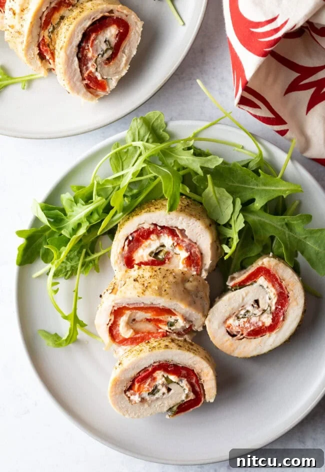 Top down view of slices of stuffed chicken roulade on a white plate with fresh arugula, highlighting the colorful filling.