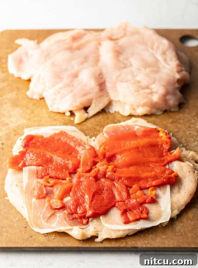 Slices of roasted red pepper laid flat on open slices of raw chicken.