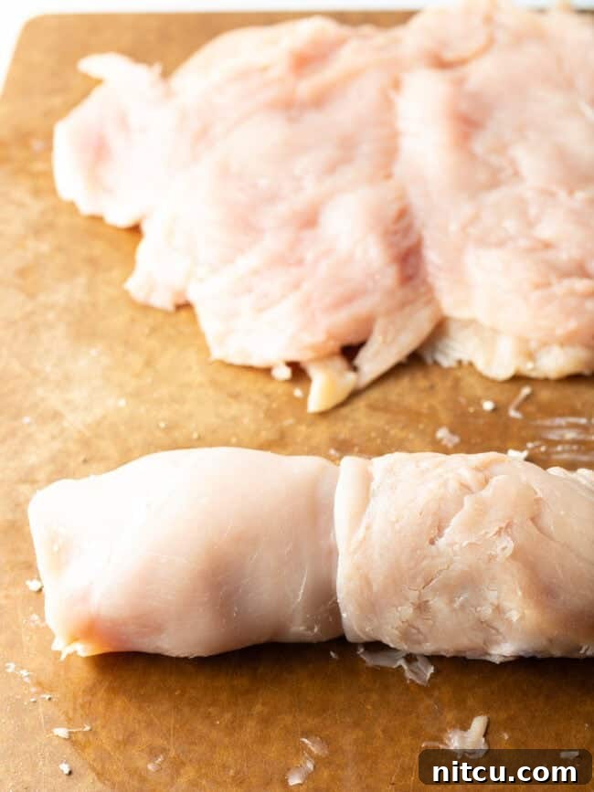 Stuffed raw chicken rolled on a cutting board, wrapped with twine for secure baking.