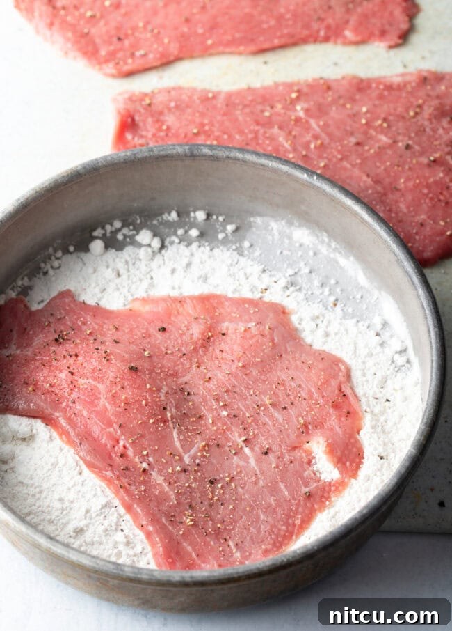 Raw cutlet in pan of flour.