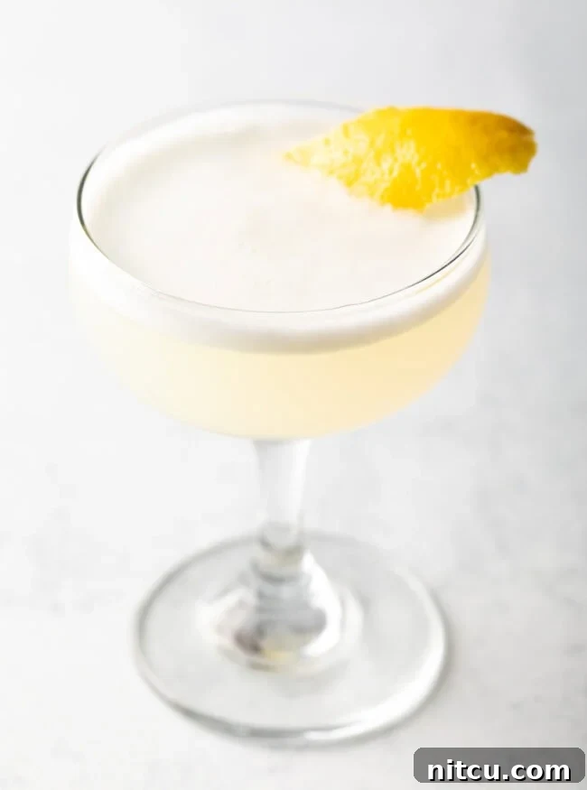 A close-up of a frothy Gin Fizz cocktail, garnished with a delicate twist of lemon, highlighting the luxurious texture and elegant presentation achieved with an egg white.