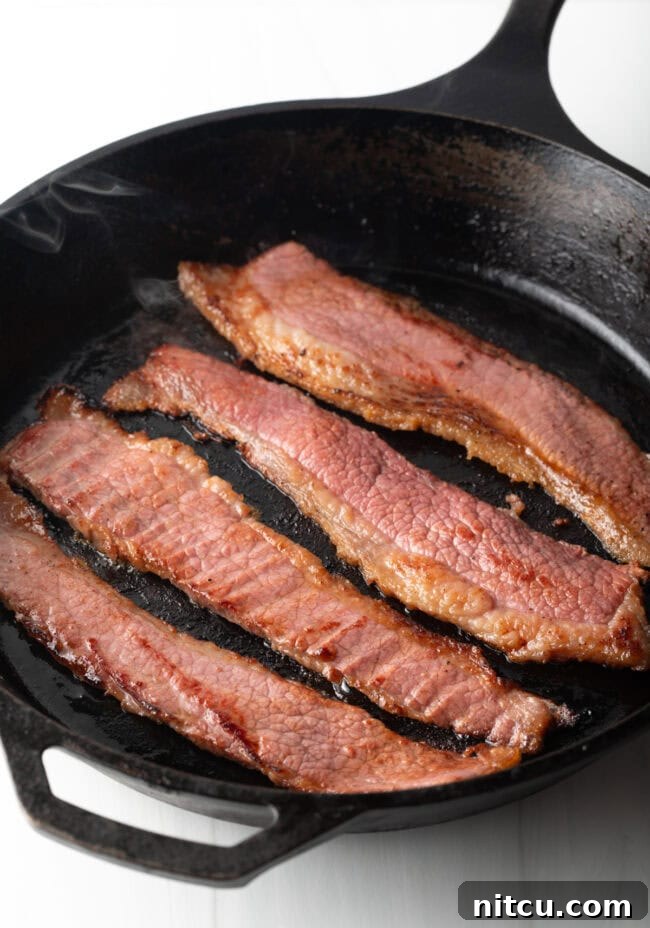 Overhead shot of 4 pieces of beef bacon in a cast iron skillet.