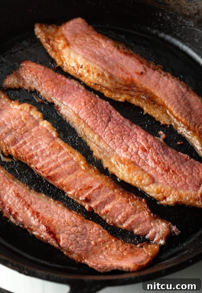 Close view of bacon cooking in a skillet.
