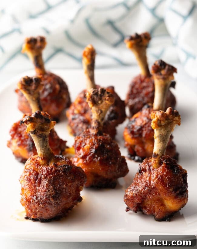 8 chicken lollipop drumettes standing up on a white serving tray.