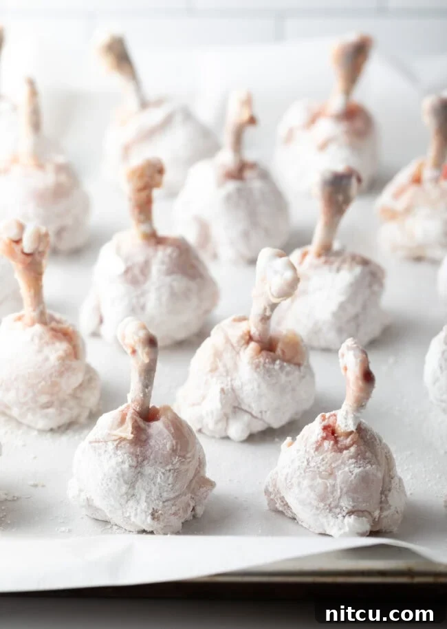 Rows of cornstarch dredged drummies on a baking sheet with parchment paper.