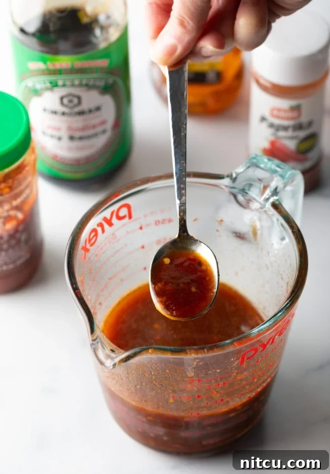 Sweet and spicy sauce made in a glass measuring pitcher, with metal spoon showing spoonful to camera.