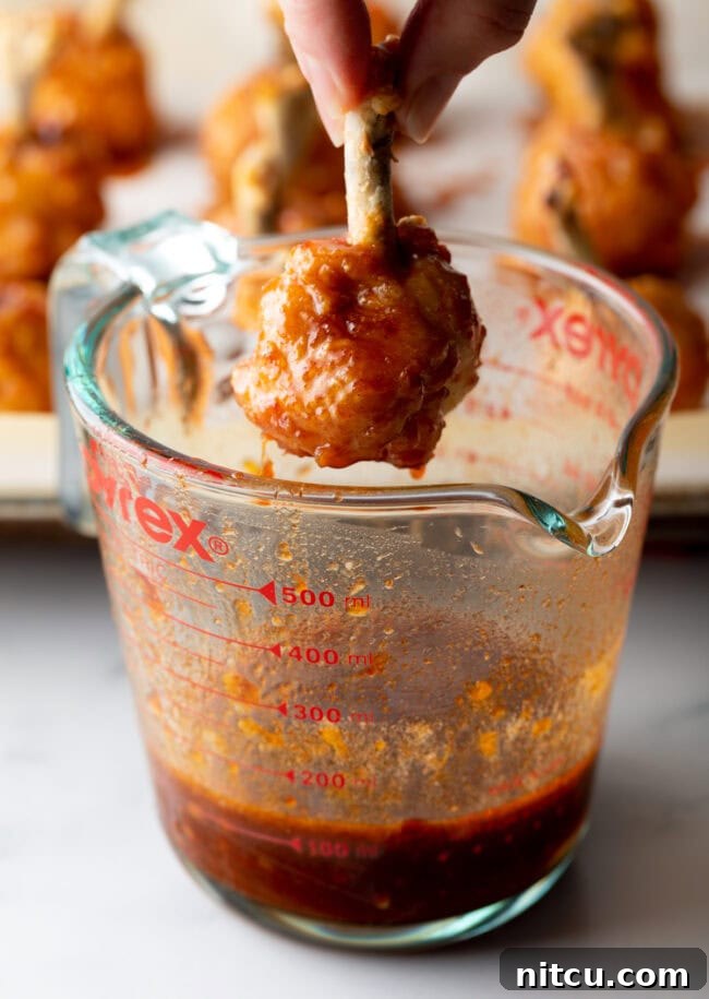 Hand dipping baked drummie into the sauce.