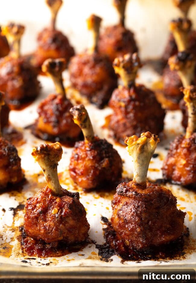 Rows of baked chicken lollipops standing straight up on a baking sheet.
