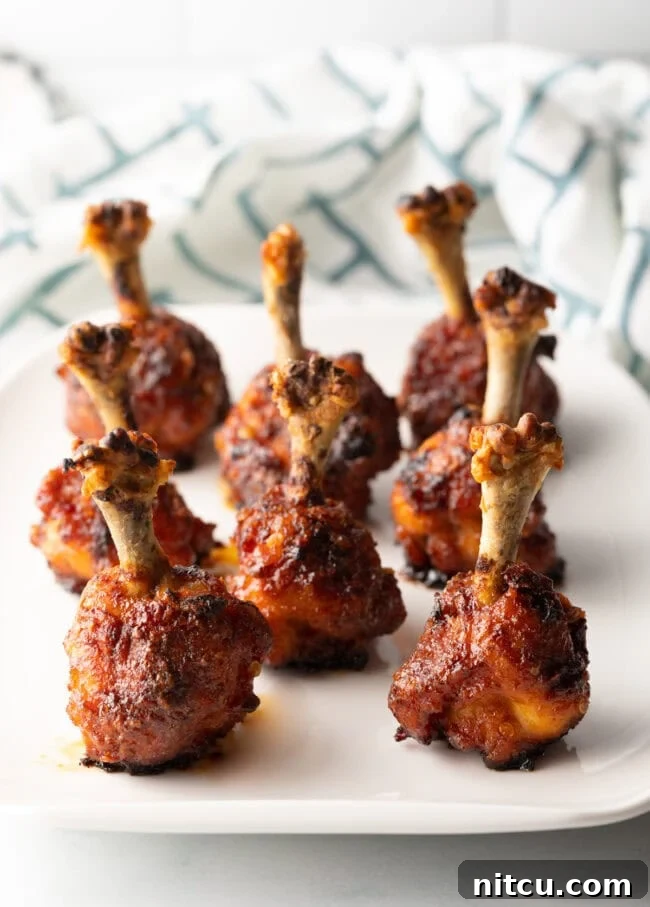 Lollipop chicken drumettes baked and standing in rows on a white serving platter.