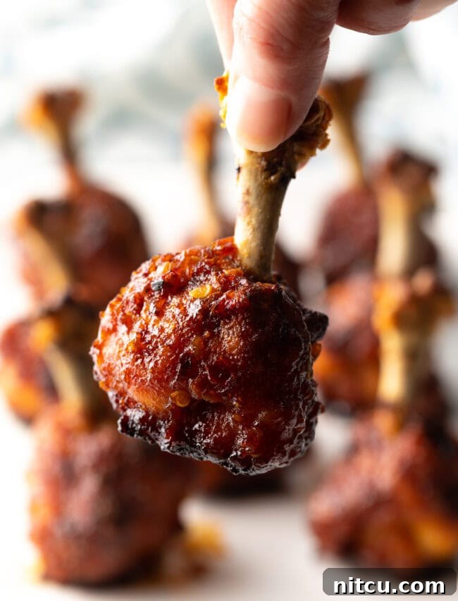 Hand holding final shot of chicken lollipop recipe, drumette to camera.