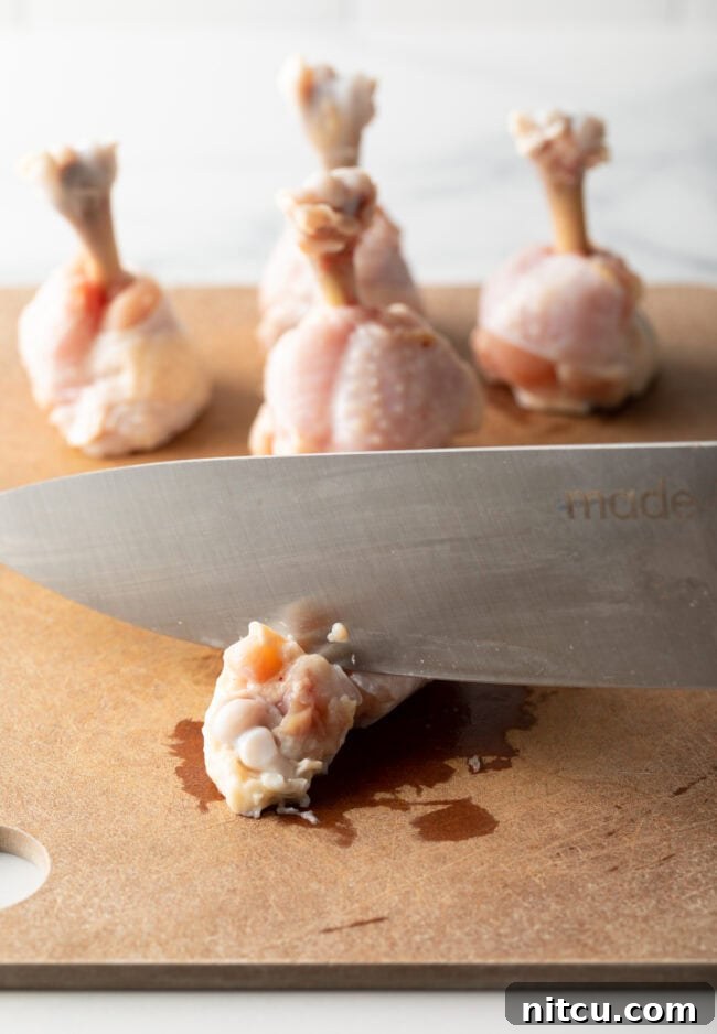 Knife cutting off tip of a drumette on a cutting board.