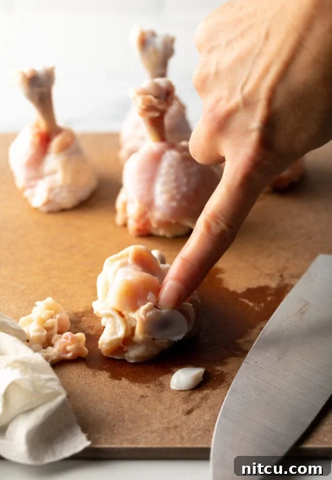 Finger pointing to tip of a drumette on a cutting board.