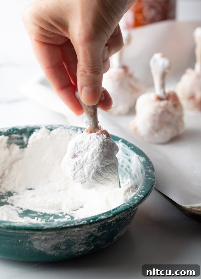 Hand dipping frenched chicken drumette into cornstarch mixture.