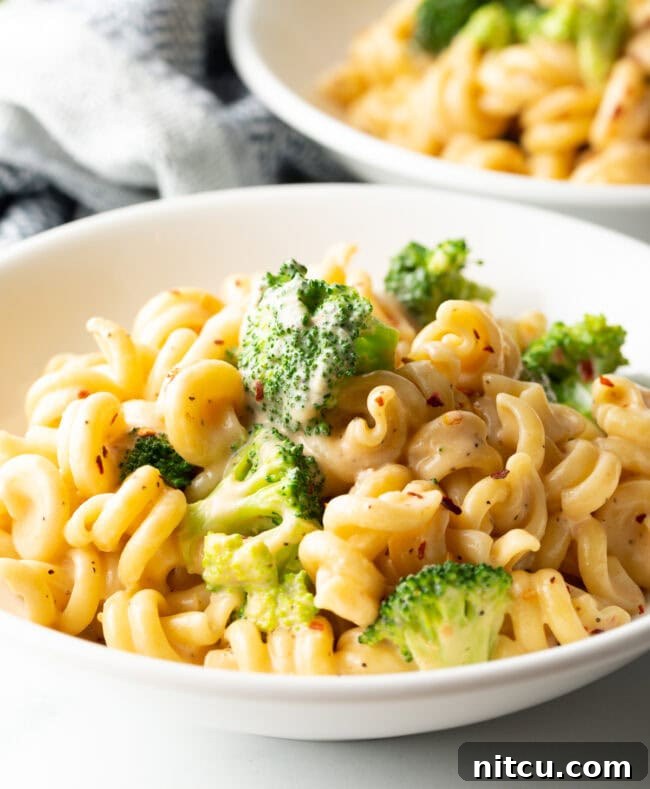 Close view white bowl with creamy cheesy broccoli pasta.