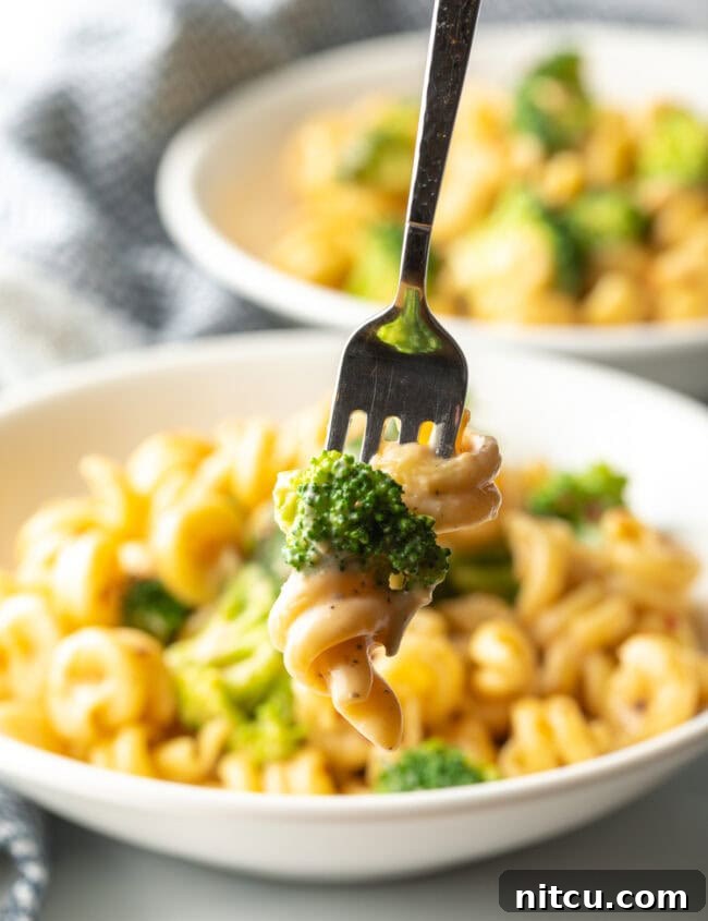 Fork with bite of boiled broccoli and cheese sauce with noodles.