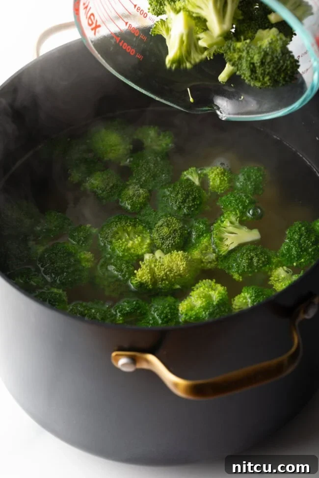 How long to boil broccoli - Fresh florets being poured from glass measuring dish into pot of boiling water.