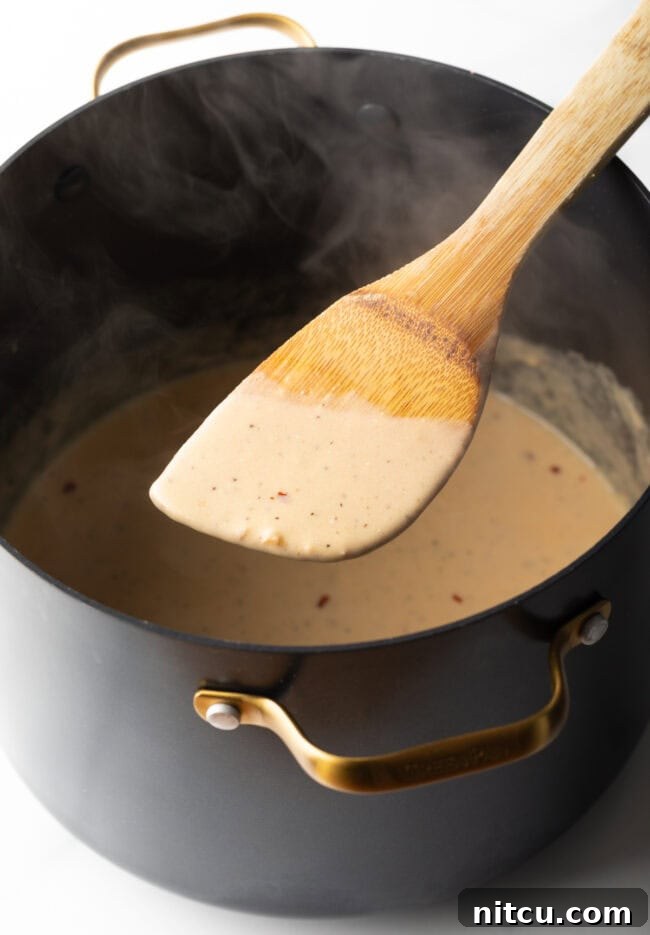 Wood spoon showing creamy cheese sauce being made in a large pot to camera.