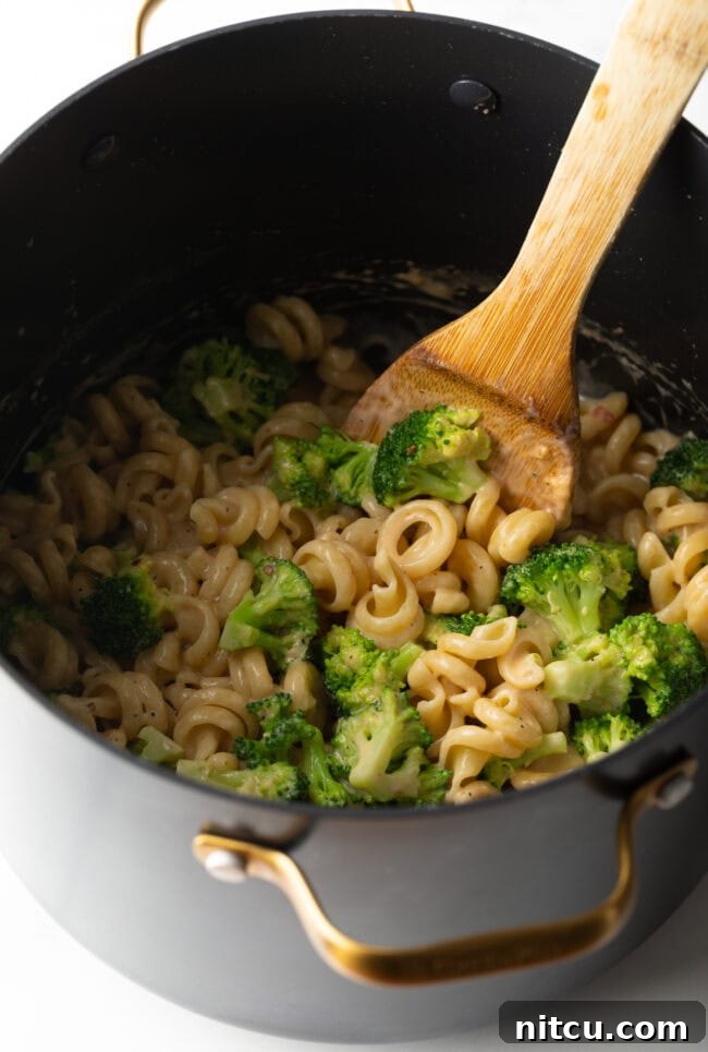 Wood spoon stirring pot with boiled broccoli, pasta, and cheese sauce.