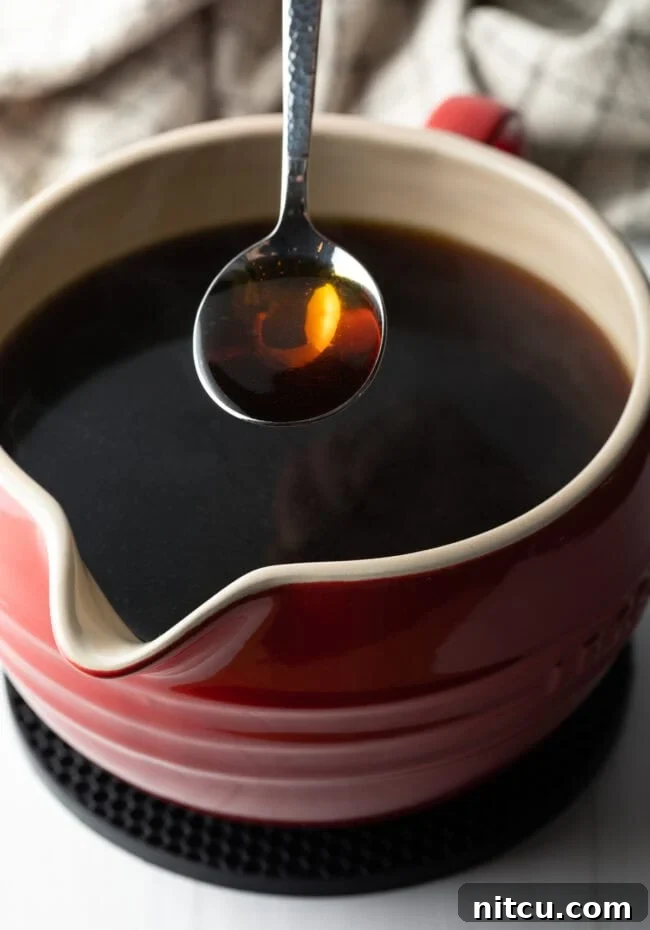 A spoon holding consomme over a ceramic bowl filled with consomme.