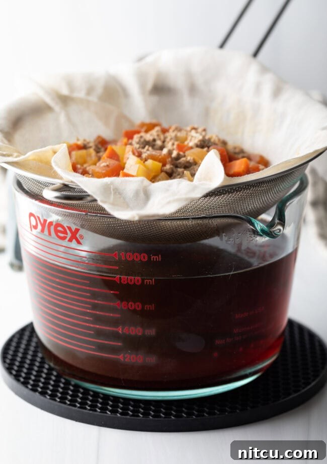 A strainer holding the consomme raft over a liquid measuring cup.