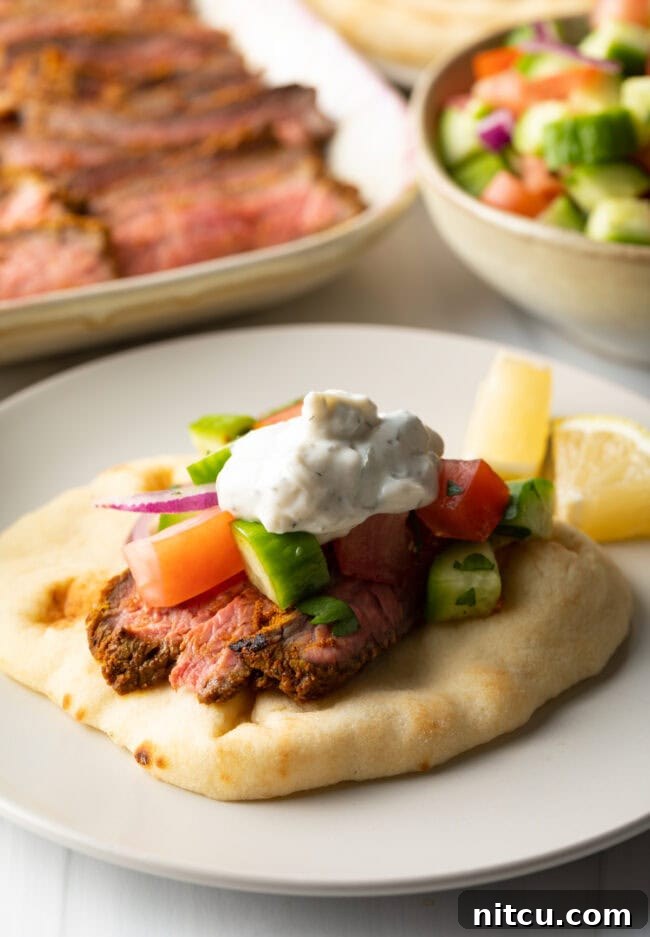 Close view flatbread naan beef shawarma wrap topped with chopped cucumbers, tomatoes, red onion and tzatziki sauce.