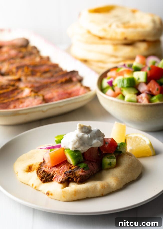 Close view flatbread naan beef shawarma wrap topped with chopped cucumbers, tomatoes, red onion and tzatziki sauce.