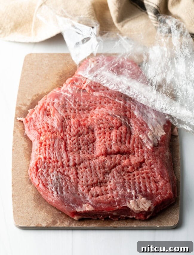 Large piece of flank steak with plastic wrap, pounded thin with a mallet.