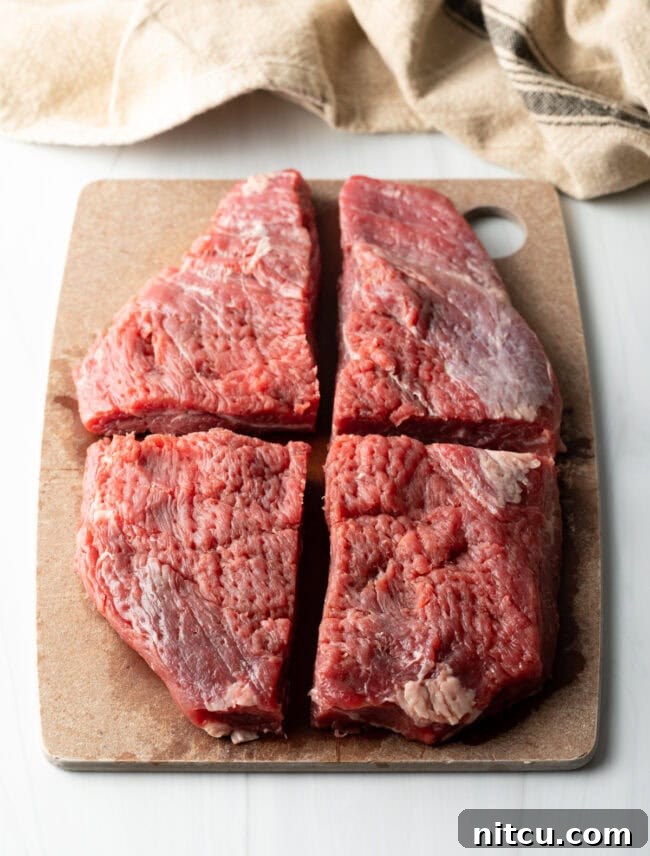 Large piece of flank steak cut into 4 quarters, on a cutting board.