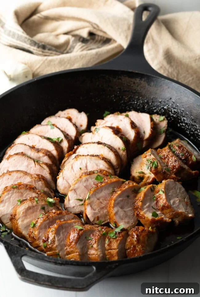 Slices of perfectly roasted honey garlic pork tenderloin glistening with glaze, elegantly arranged in a black cast iron pan, ready to serve.
