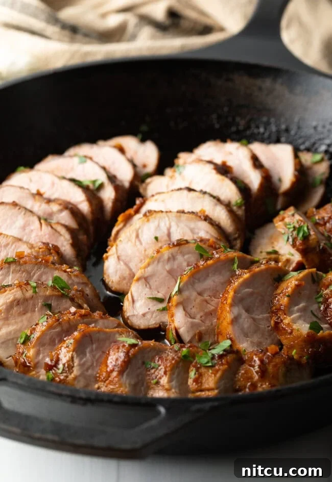 Close-up of succulent slices of slow cooker honey garlic pork tenderloin, served in a black cast iron pan, showing the rich glaze.